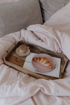 A cozy breakfast in bed scene with a croissant and coffee on a wooden tray.