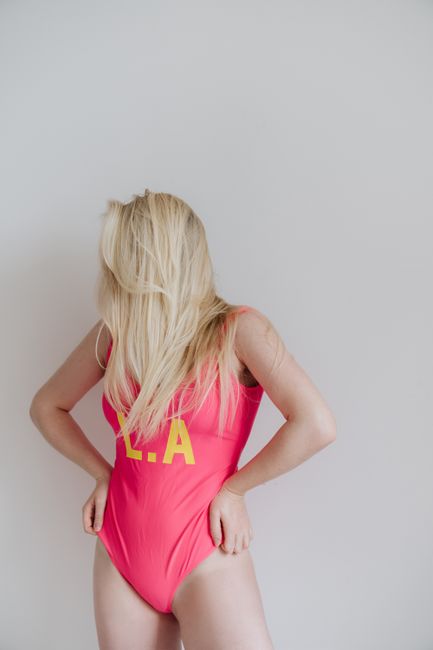 Stylish blonde woman posing in pink swimsuit with L.A. print, indoors, fashion and swimwear theme.