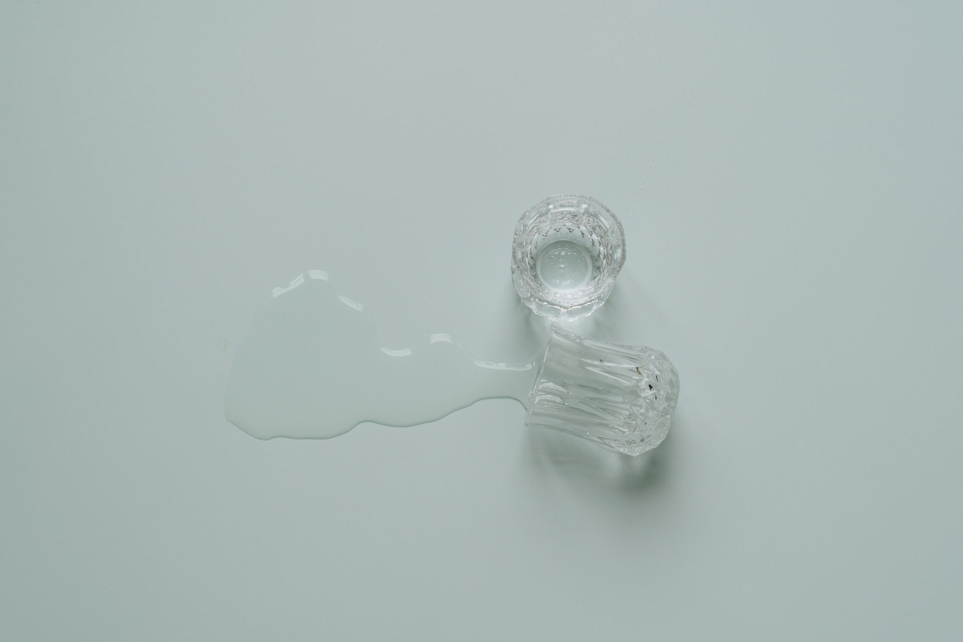 A clear glass tumbler spilled on a flat surface, creating a minimalist and serene scene.