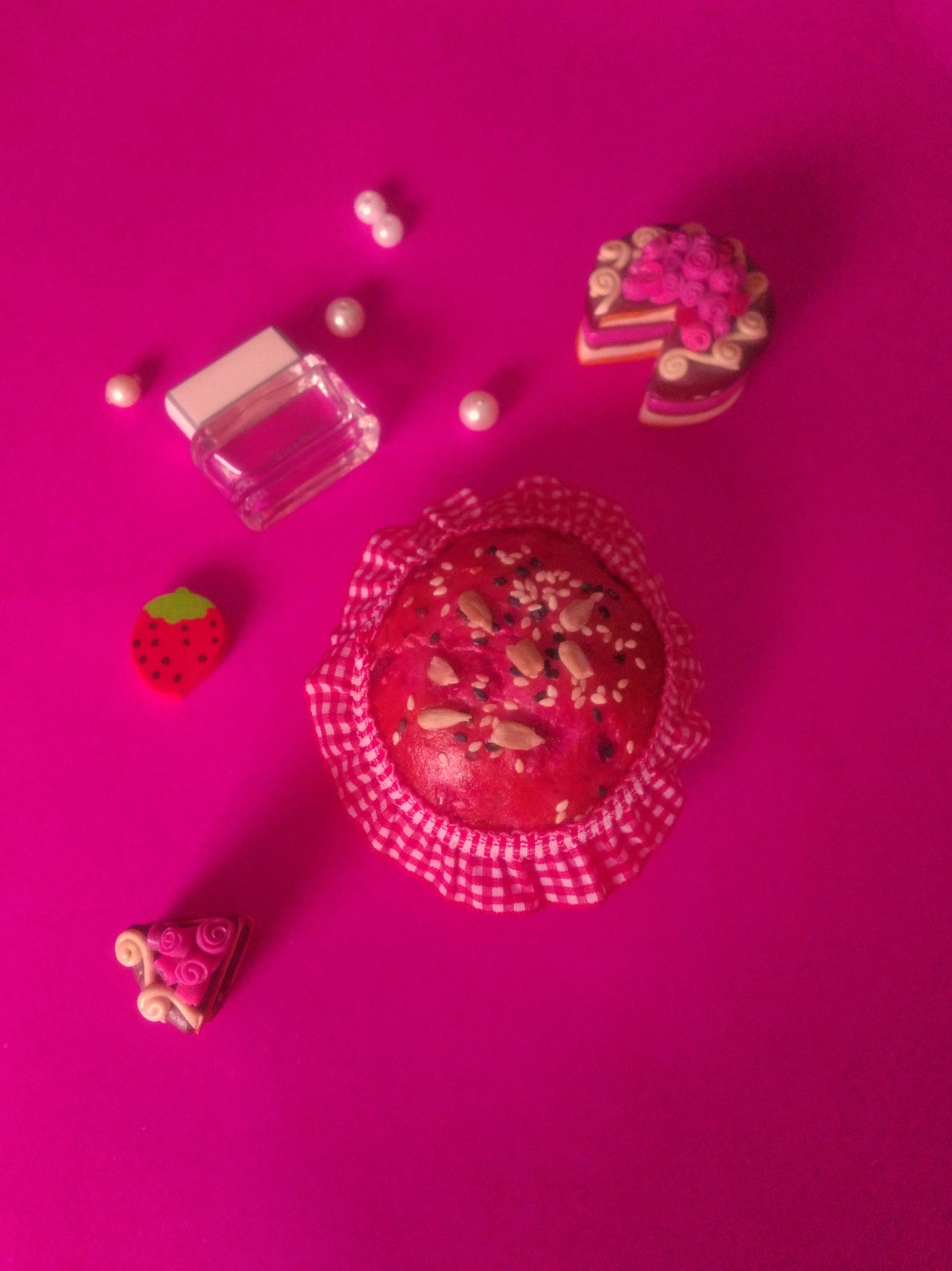 Vibrant pink flat lay featuring a berry muffin with sprinkles and decorative sweets.