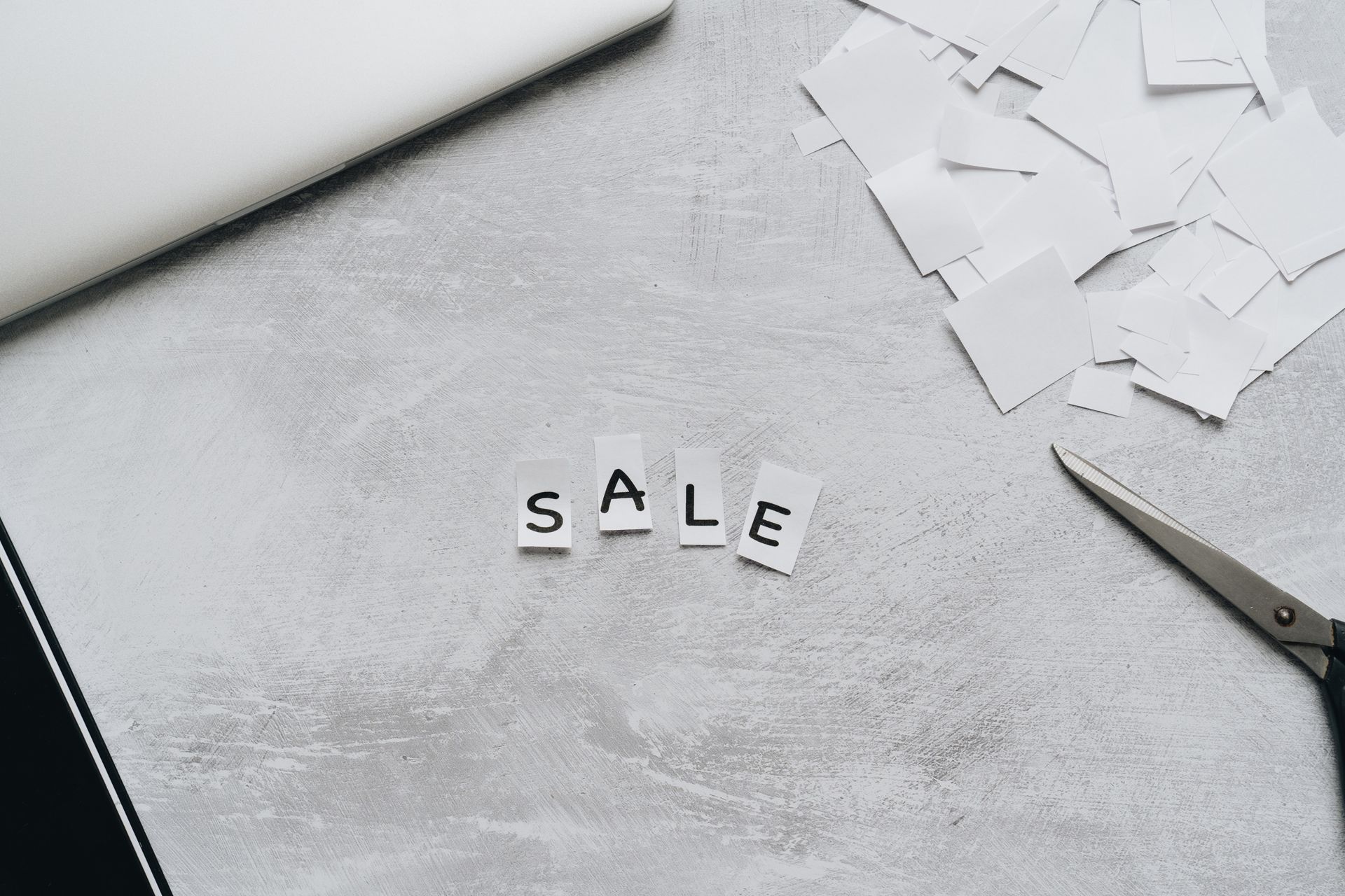 Overhead view of cut-out letters spelling 'Sale' on a desk with scattered paper and scissors.