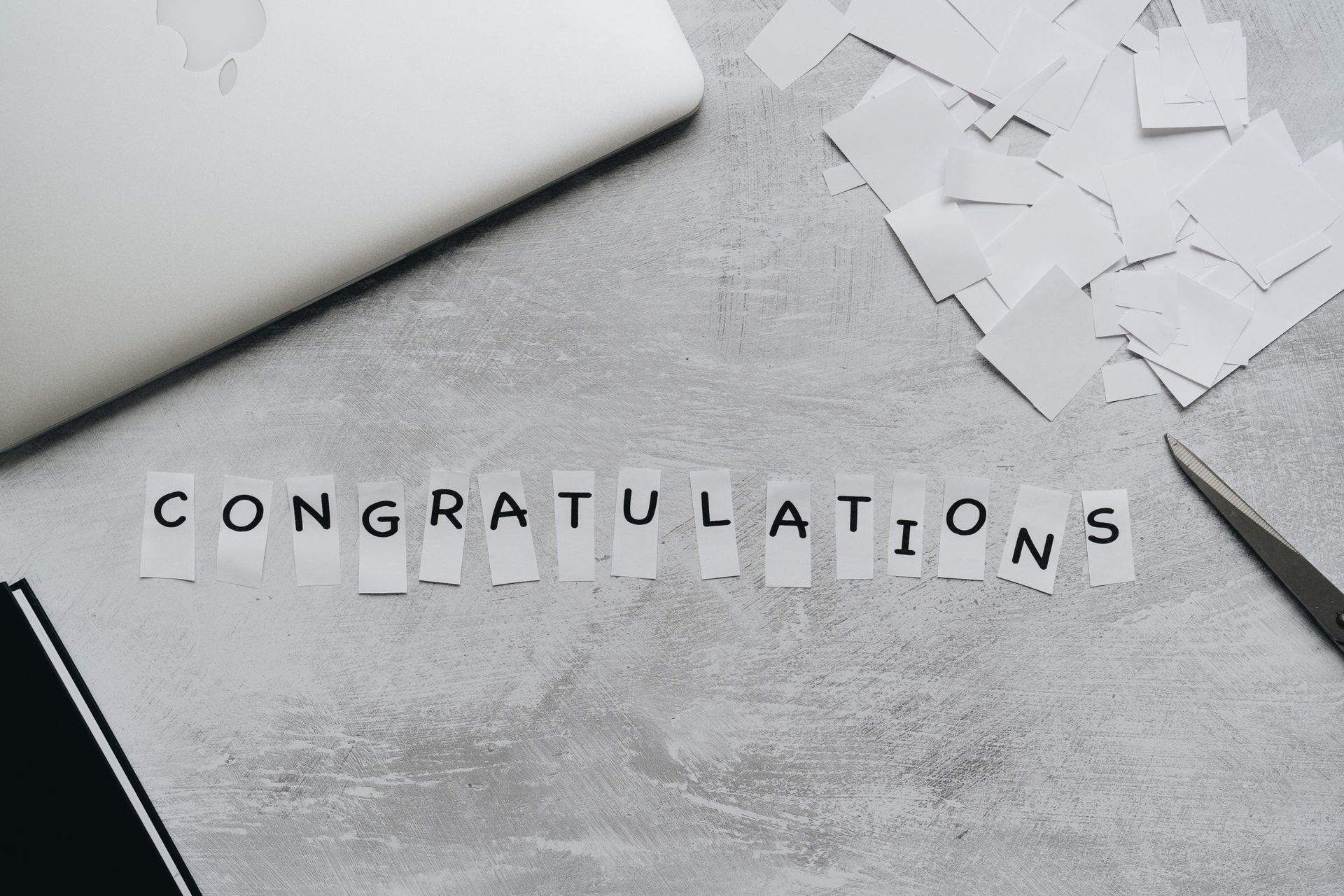 Creative layout of congratulations message using cutout letters on desk with laptop.