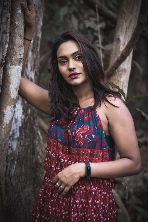 Free A woman in a floral dress poses confidently against a tree in an outdoor setting. Stock Photo