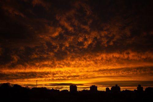 Free Silhouettes of contemporary town buildings located under majestic cloudy sunset sky of bright orange color Stock Photo