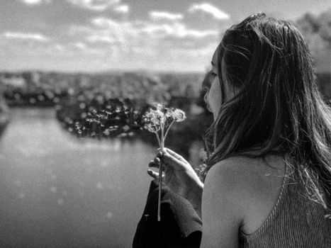 Black and white image of a woman blowing dandelions over a river.