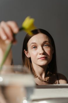 柔和灯光下，一个女人在室内拿着玻璃花瓶里的一朵黄花