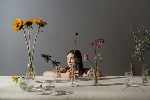 一个坐在玻璃花瓶后面的女人，展示着各种鲜花的创造性花卉展示
