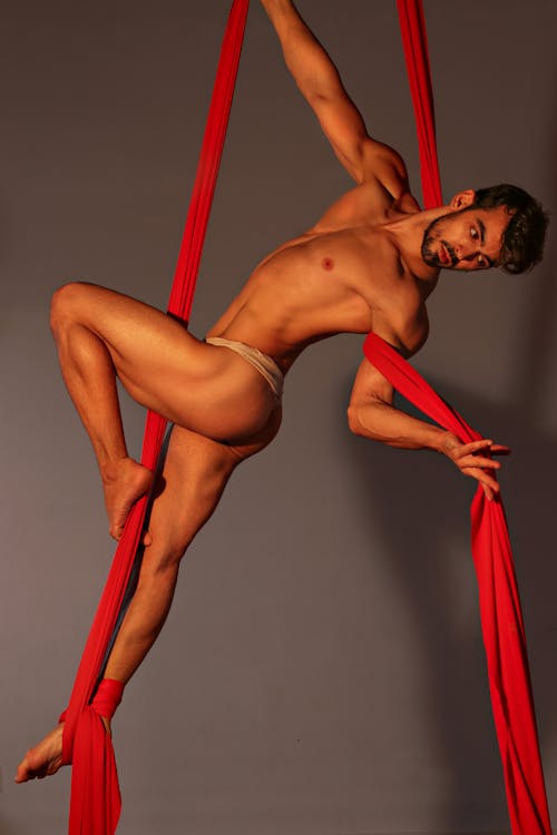 Strong sportsman practicing aerial gymnastics on silks
