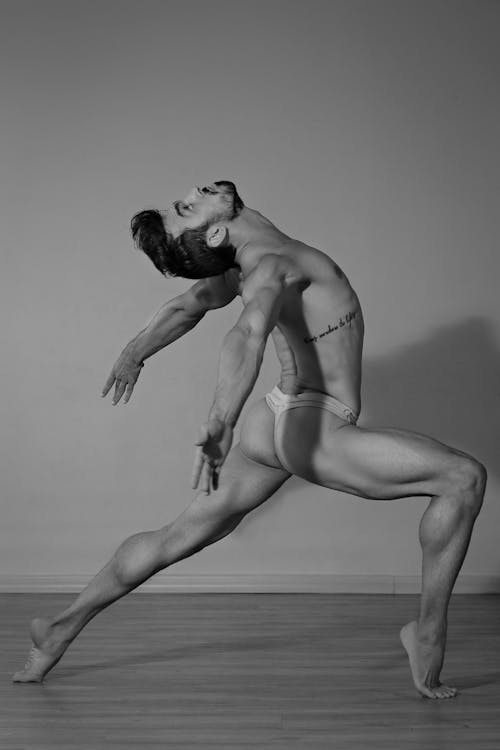 Black and white side view full length flexible masculine male acrobat in men panties performing in dance studio