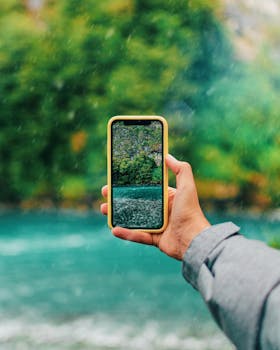 A hand holds a smartphone capturing a scenic view in Puerto Varas, Chile.
