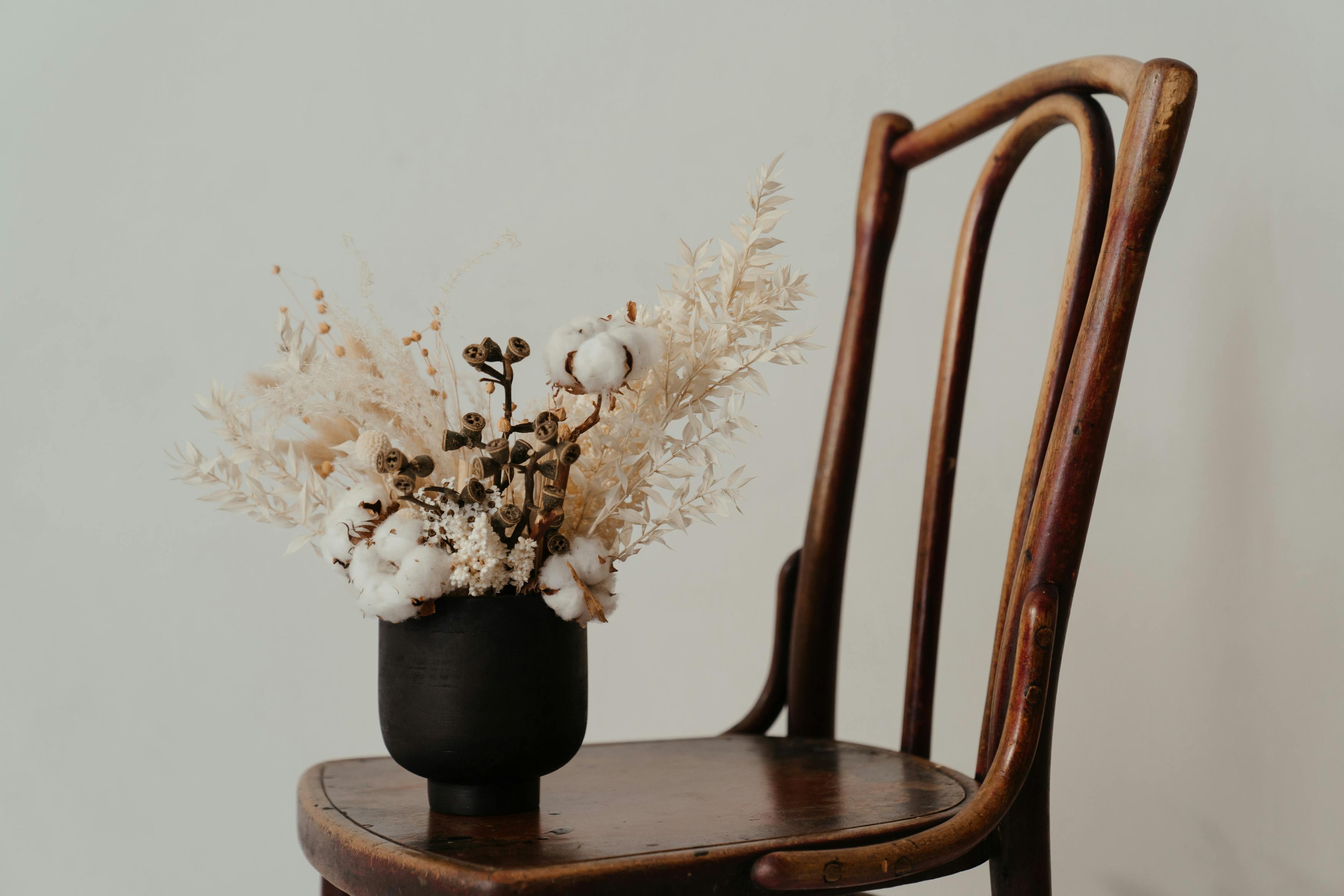 white flowers in black ceramic vase on brown wooden chair
