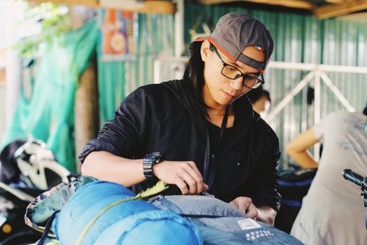Positive young ethnic male in casual wear and hat preparing backpacks before travelling while standing on sunny backyard