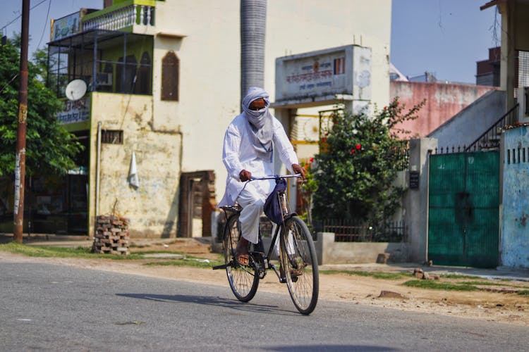 Unrecognizable Asian Man In White Clothes Riding Bicycle Along Street