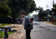Serious ethnic father piggybacking daughter on poor district street