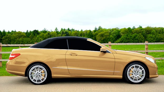 A sleek gold convertible parked outdoors against a lush green backdrop.