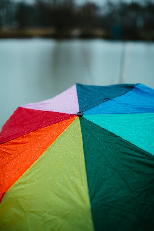 From above of multicolored umbrella with rain drops against blurred background of water surface