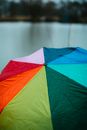 透过五彩的雨伞望去，雨滴映在模糊的水面背景上