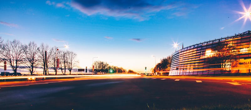 Wide angle of contemporary city buildings located near leafless trees on embankment in dusk