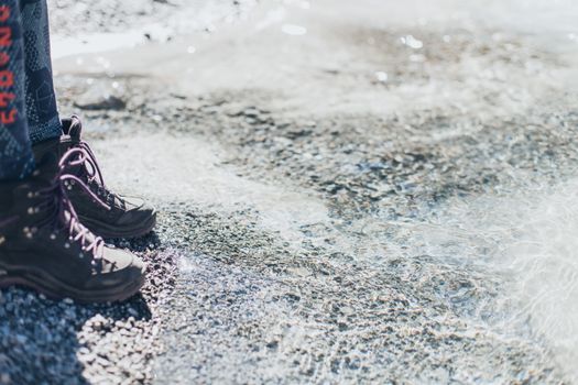 Unrecognizable person in boots standing on ground near frozen clean surface at daytime