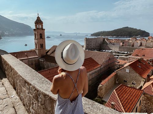 Free A woman in a hat enjoys a scenic view of Dubrovnik, Croatia with historic buildings and the sea. Stock Photo