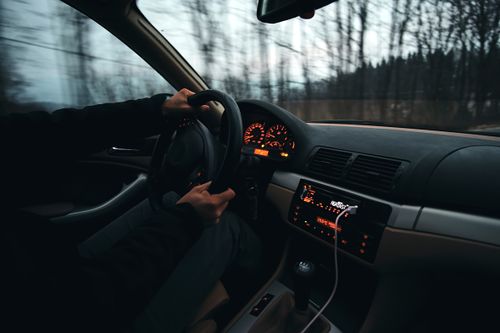 Free Close-up of a person driving a stylish car through a scenic, blurred outdoor view. Stock Photo