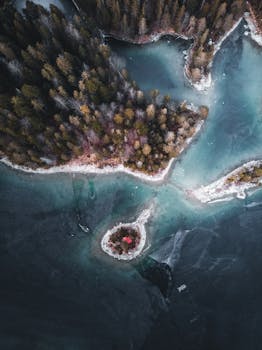 Drone view of a frozen lake surrounded by forest in Grainau, Germany, showcasing winter's beauty.