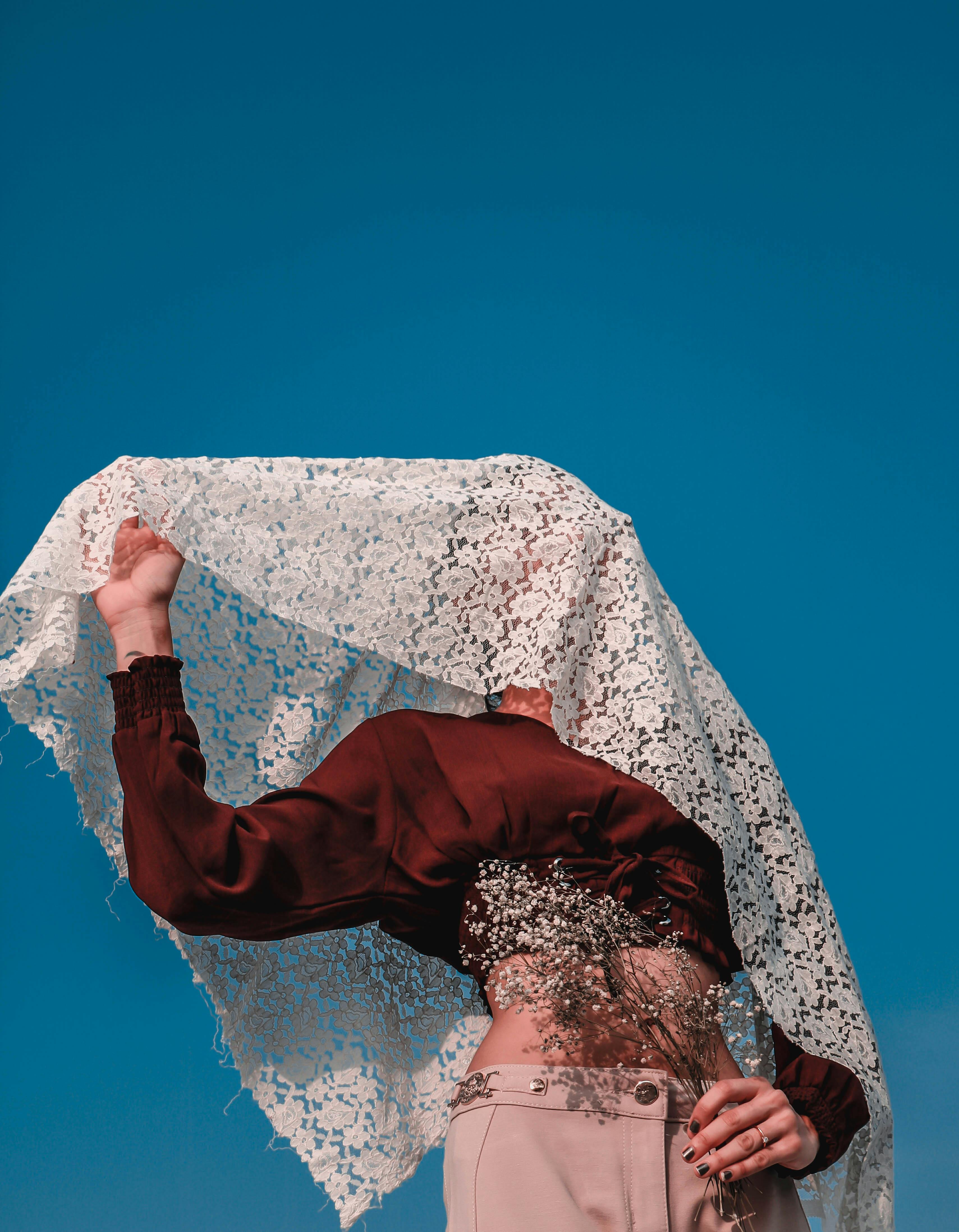 一位优雅的女人戴着蕾丝面纱，在清澈的蓝天下散发着神秘与时尚