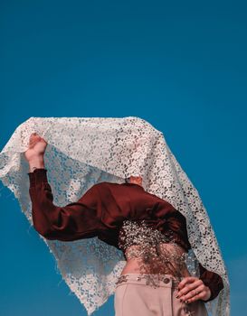 一位优雅的女人戴着蕾丝面纱，在清澈的蓝天下散发着神秘与时尚