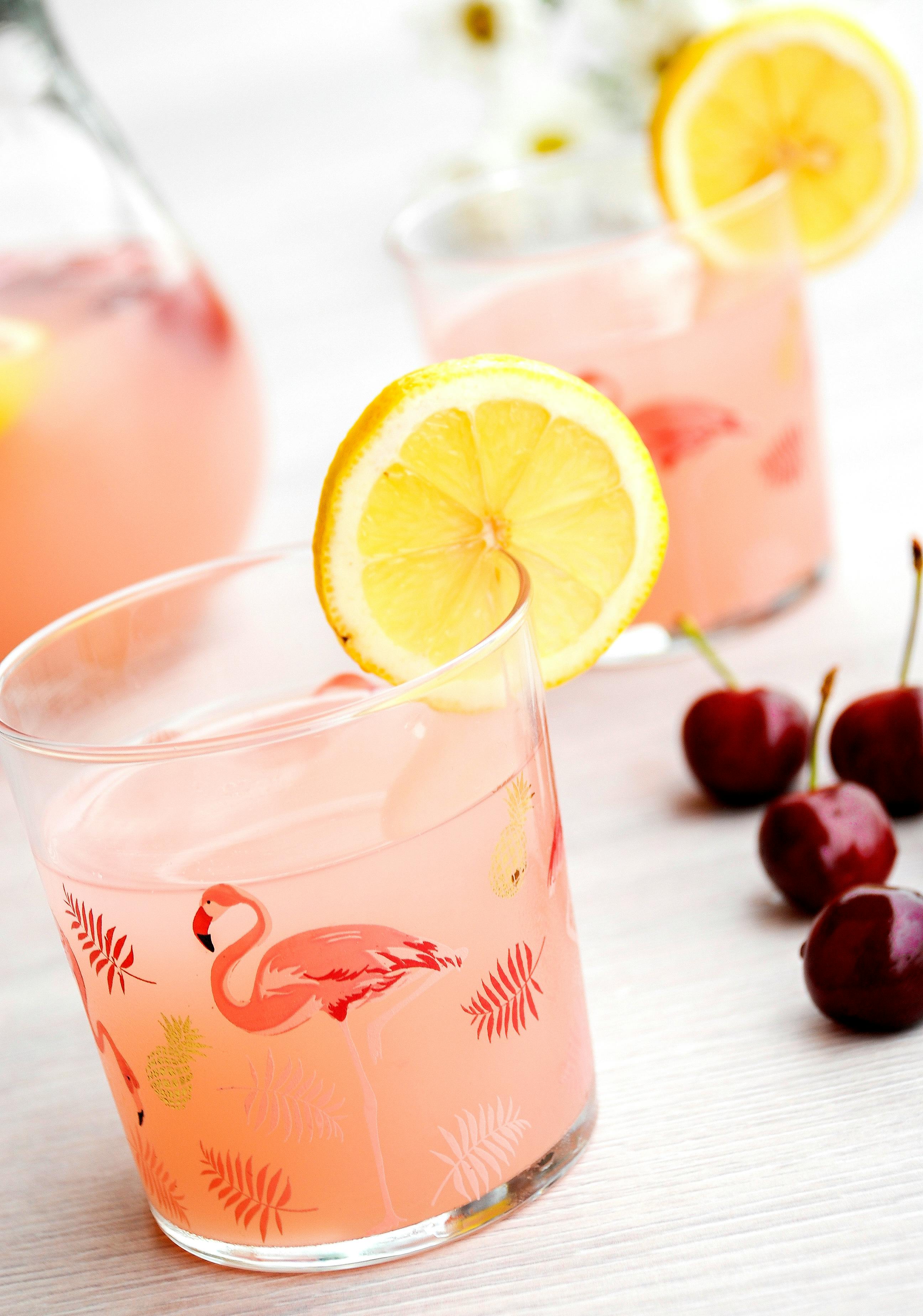 A vibrant glass of pink lemonade with lemon slices and cherry garnish, perfect for summer refreshment.