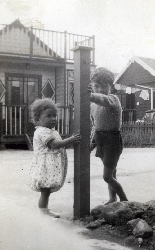 Free Two children playing near a post in an outdoor vintage black and white scene with houses in the background. Stock Photo