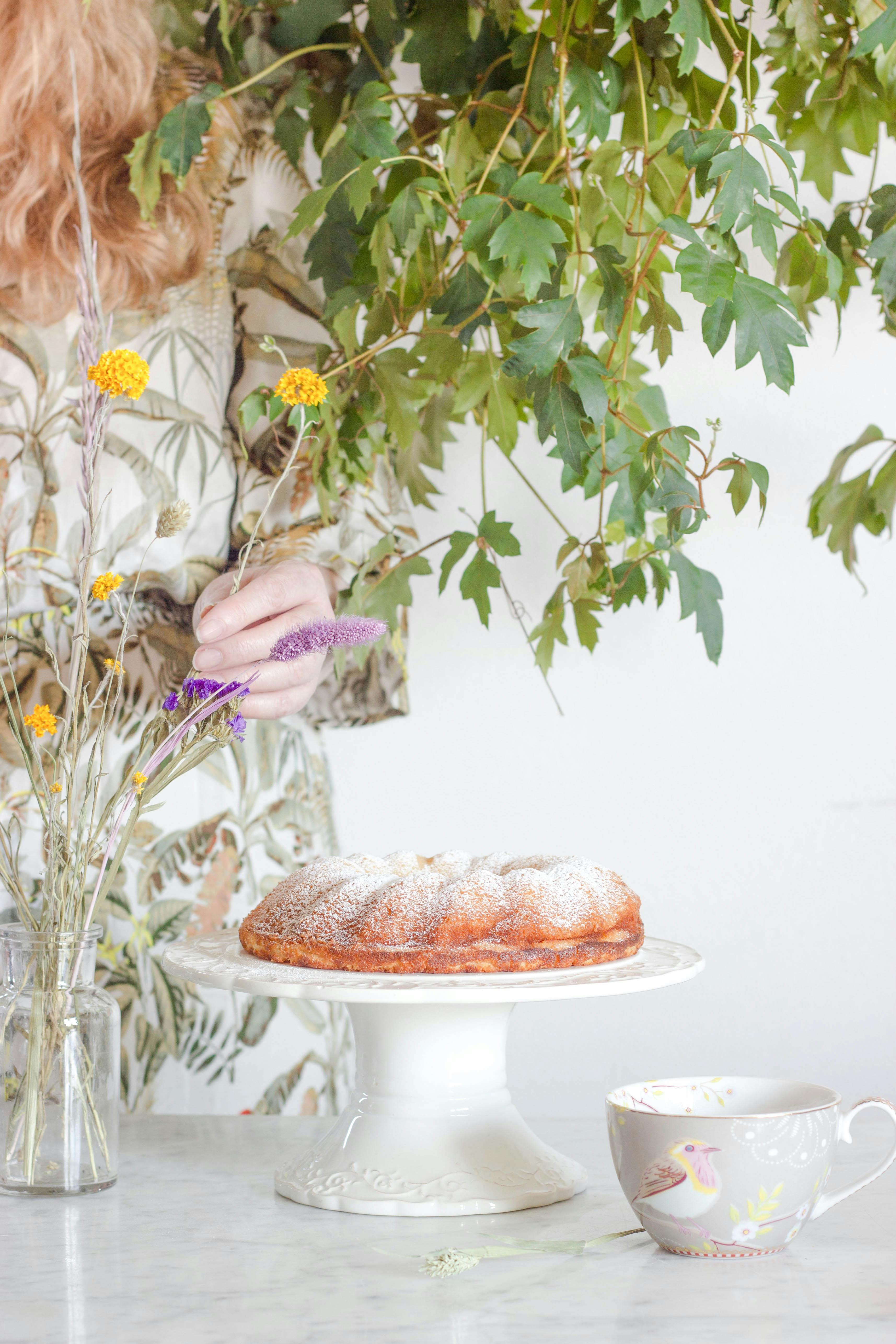 A cake on a stand surrounded by wildflowers and teacup, creating a rustic and cozy atmosphere.