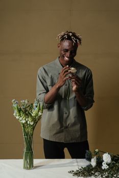 留着辫子的男人在室内花瓶旁拿着鲜花微笑
