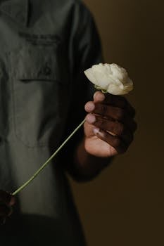 Elegant close-up shot of a hand holding a delicate white ranunculus flower against a dark background.