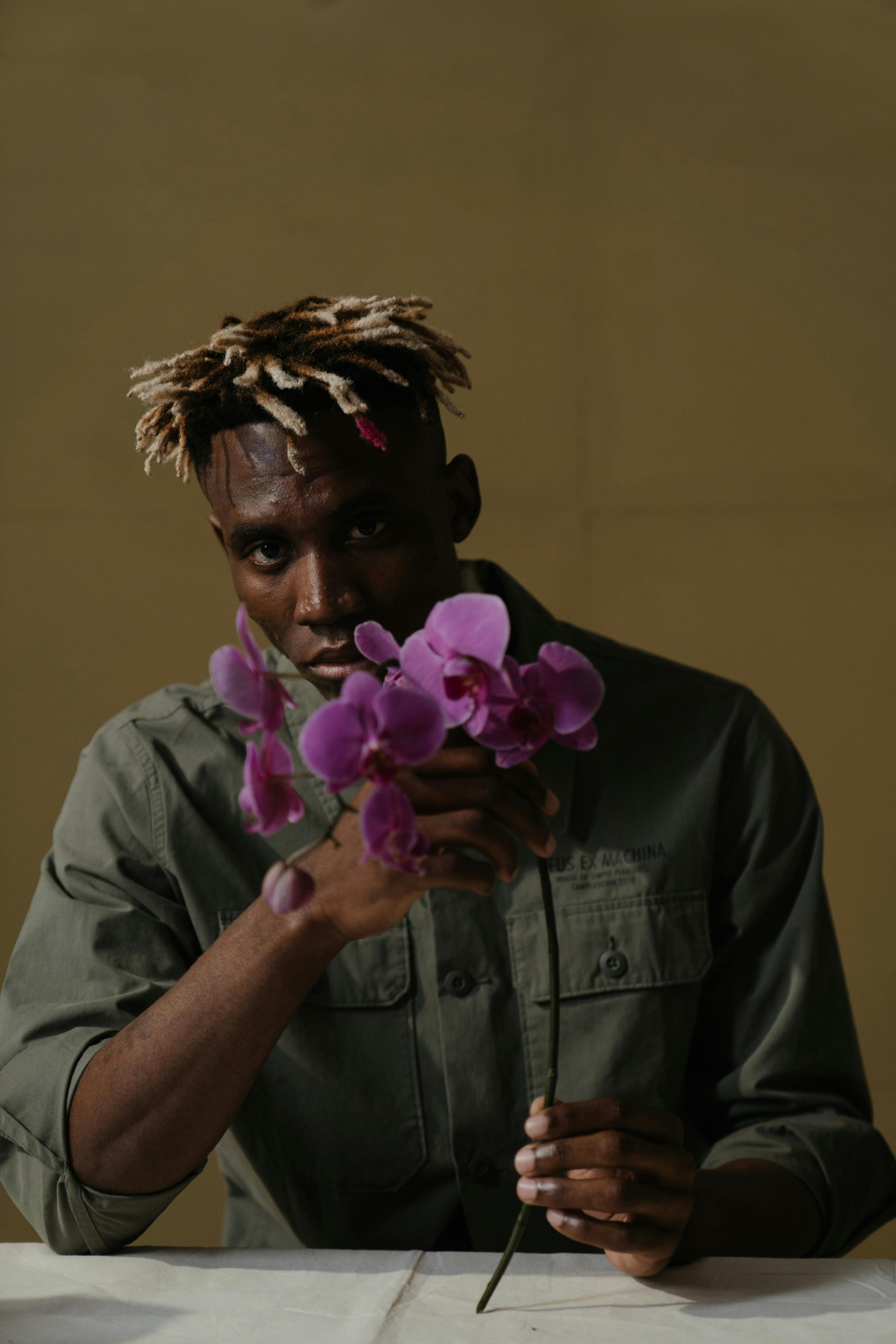 一名男子在室内手持一束充满活力的紫色兰花，表情沉思