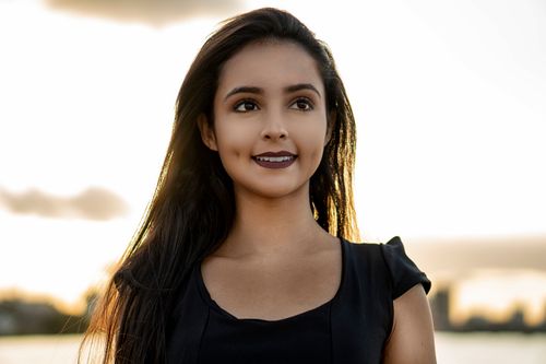 Free Charming portrait of a brunette woman smiling warmly as she gazes away, set against a soft outdoor background. Stock Photo