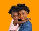 Young African American female holding little girl on hands looking tenderly at camera on orange background