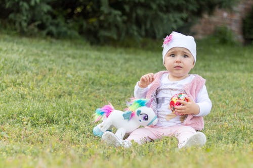 Upset baby on green meadow with toys