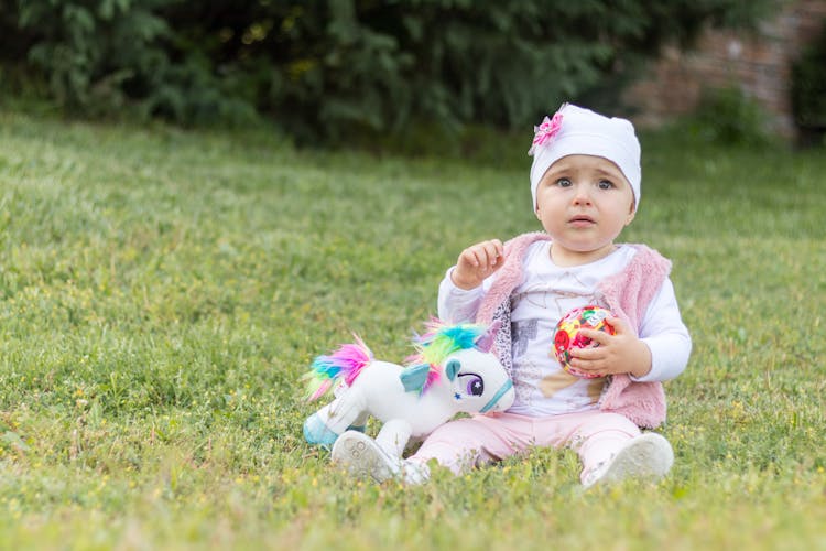 Upset Baby On Green Meadow With Toys