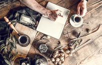 Crop person writing in notepad at rustic table