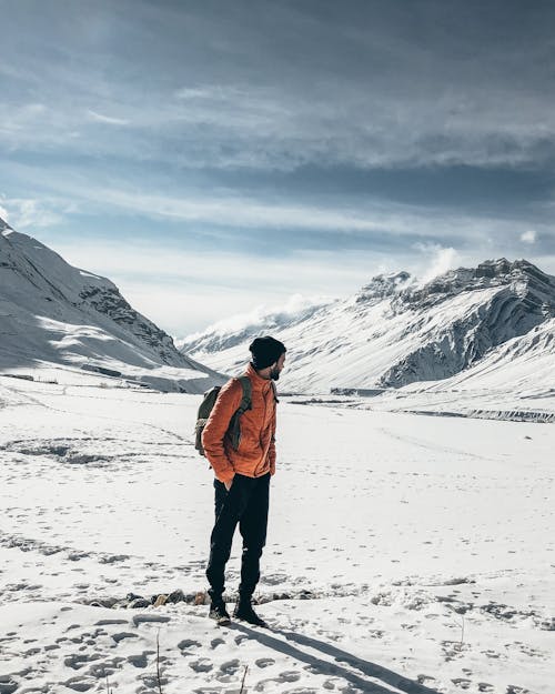 Full body hiker in outerwear and with backpack observing majestic mountains in snow