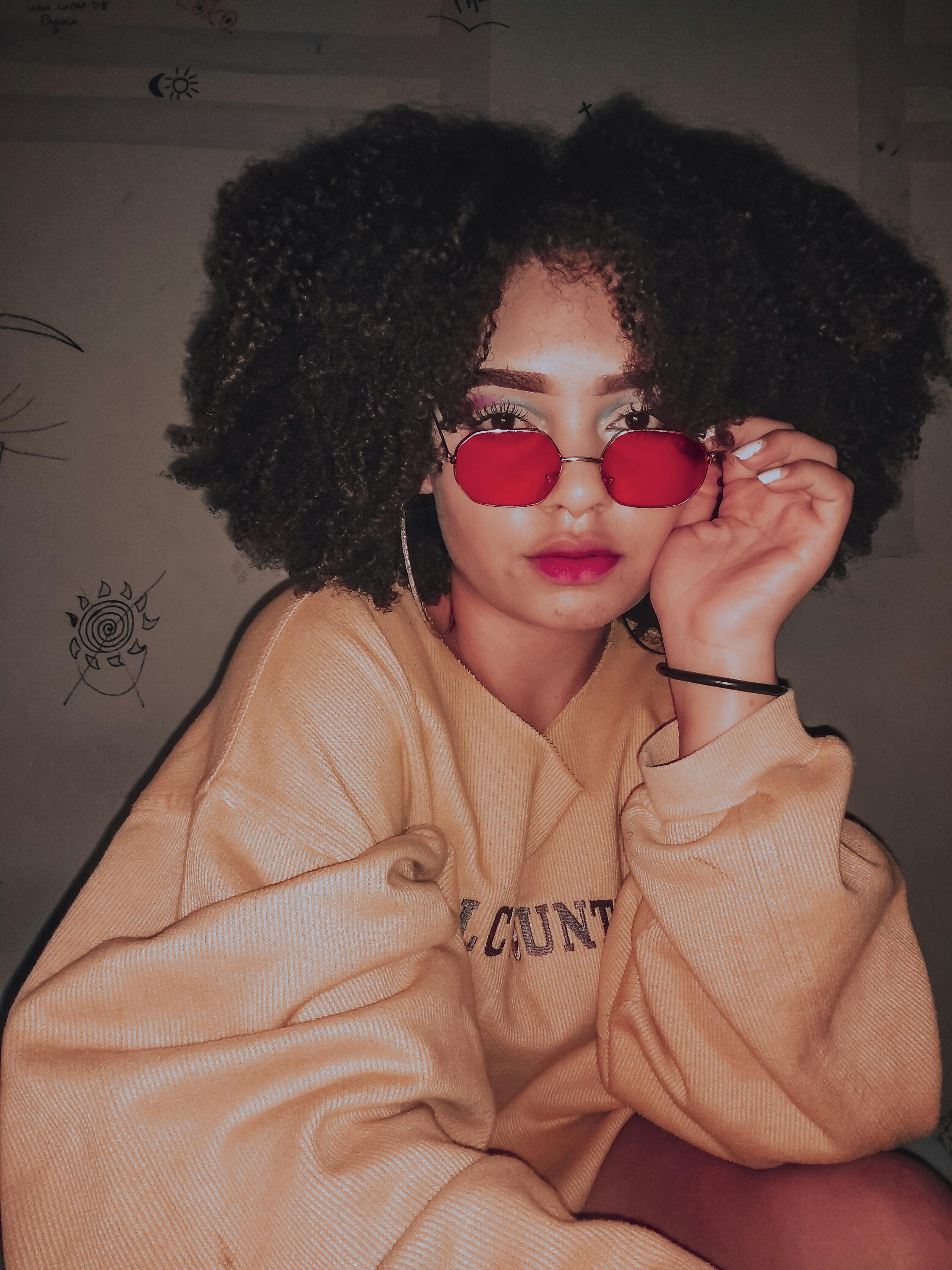 Young black woman with Afro hairstyle wearing hoodie and pink sunglasses looking at camera