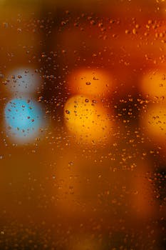 Raindrops on a window with colorful city lights bokeh creating a serene, abstract ambiance.