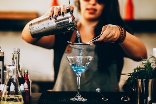 Free A bartender pouring a vibrant blue cocktail through a strainer into a glass. Stock Photo