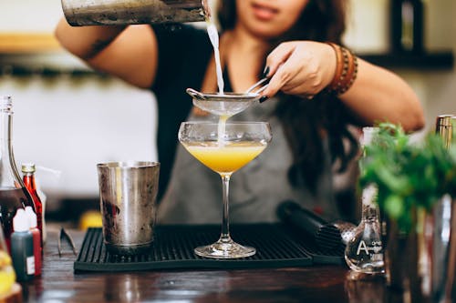 Crop woman mixing colorful liquids while preparing alcoholic drink