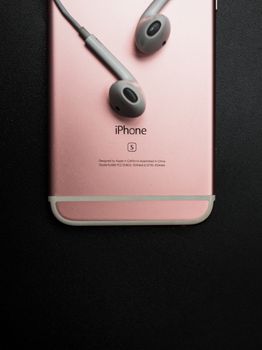 Close-up of rose gold smartphone with earphones on a black background, highlighting modern technology.