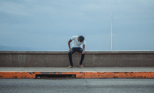Photo of Man Sitting on Concrete Wall Barrier