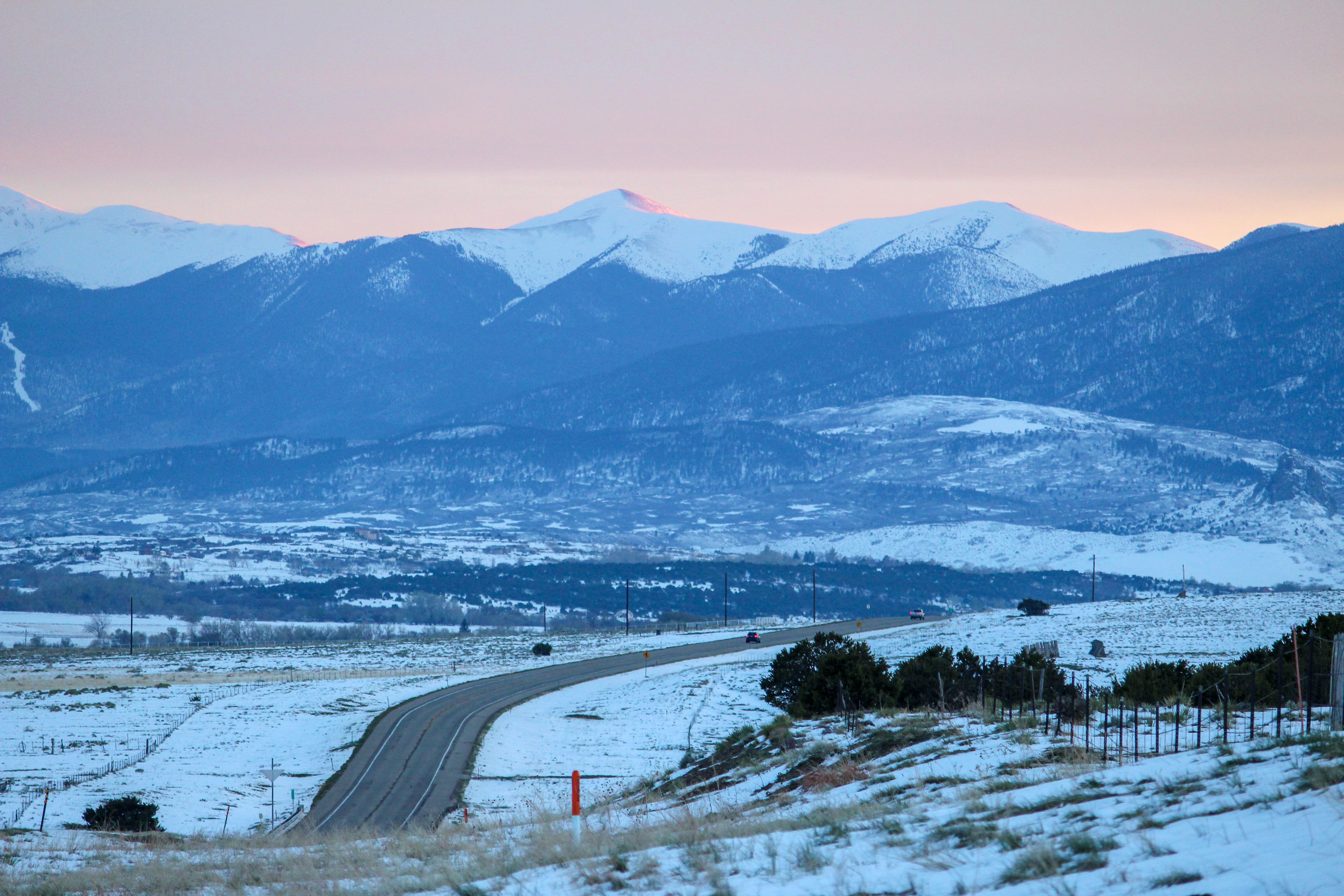 Snow-covered road winding through the winter landscape of Crested Butte, Colorado with mountain views at sunset.