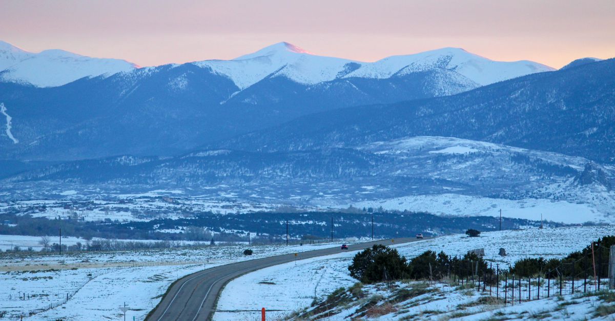 Snow-covered road winding through the winter landscape of Crested Butte, Colorado with mountain views at sunset.