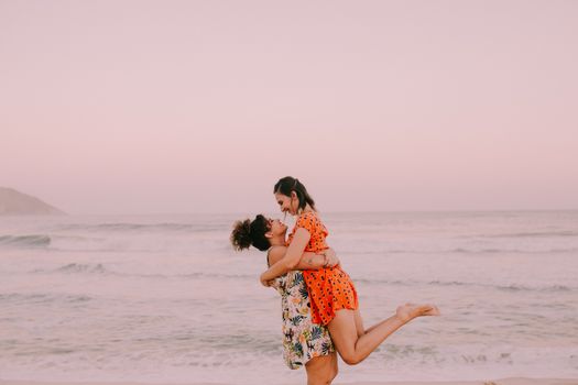 一对快乐的女同性恋夫妇在日落时分的海边相拥，创造了一个充满爱意和亲密的时刻