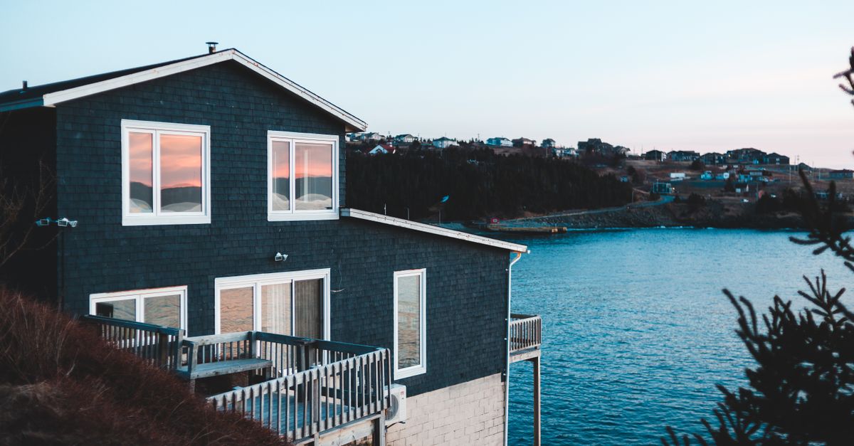 Brick building with fenced terrace and windows reflecting sky on mountain near growing trees and rippled ocean at sundown